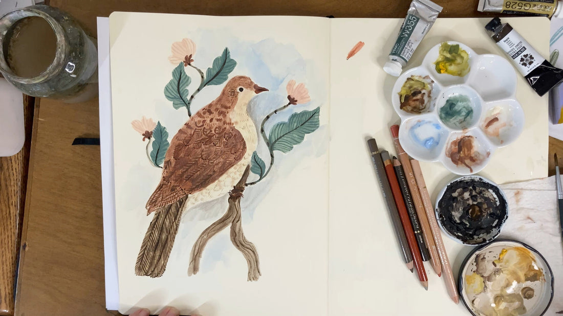 An overhead view of a bird painting in a sketchbook, with art supplies, paint water and paints.